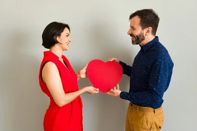 Couple joyfully holding a heart-shaped paper cutout, symbolizing love and affection between them.