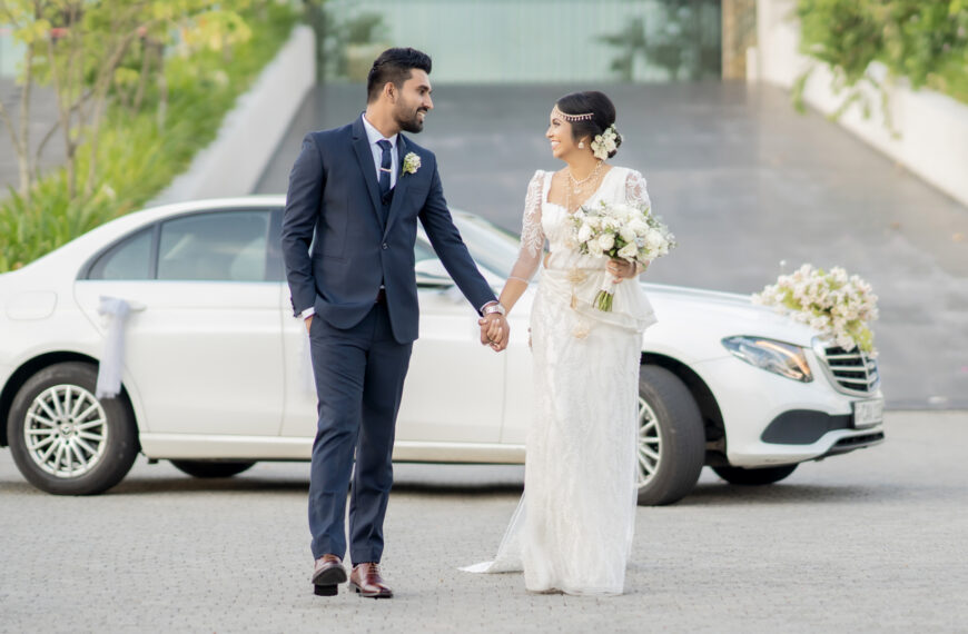 A bride and groom in beautiful wedding outfits, holding hands and smiling, standing in front of a decorated white car on their wedding day, mangala yojana 2024, matrimony sri lanka, sl marriage proposals, mangala yojana, marriage proposal in sri lanka, sri lankan matrimony, sri lankan marriage proposal sites