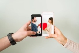 Two people smiling while holding up their phones, each displaying a heart symbol on the screen.