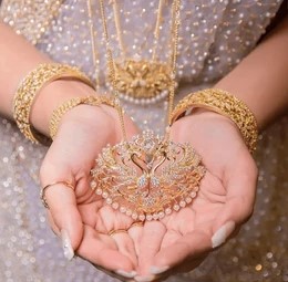 A woman displays a gold necklace and bracelet, showcasing their elegant design and shine.