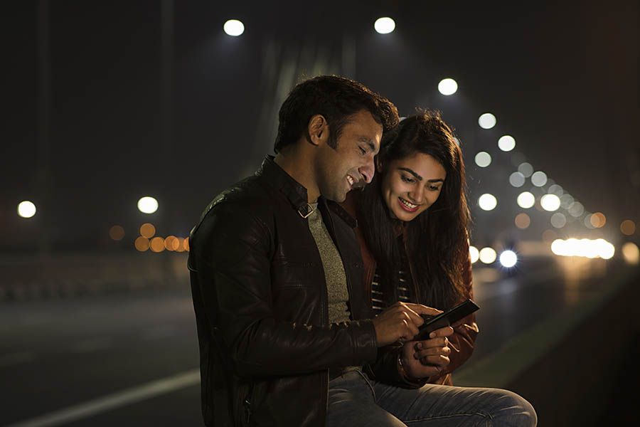 A man and woman sit together on a bridge at night, surrounded by soft lighting and a serene atmosphere.