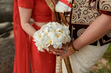 A couple in traditional Sri Lankan attire holding a bouquet of white flowers, wearing ornate embroidered clothing in a celebratory and intimate wedding setting, symbolizing poruwa ceremony traditions, Sri Lankan matrimony, marriage proposals in Sri Lanka, mangala yojana, buddhist matrimony, catholic marriage proposals, and secure matchmaking through Poruwa.lk for Lanka brides and grooms.