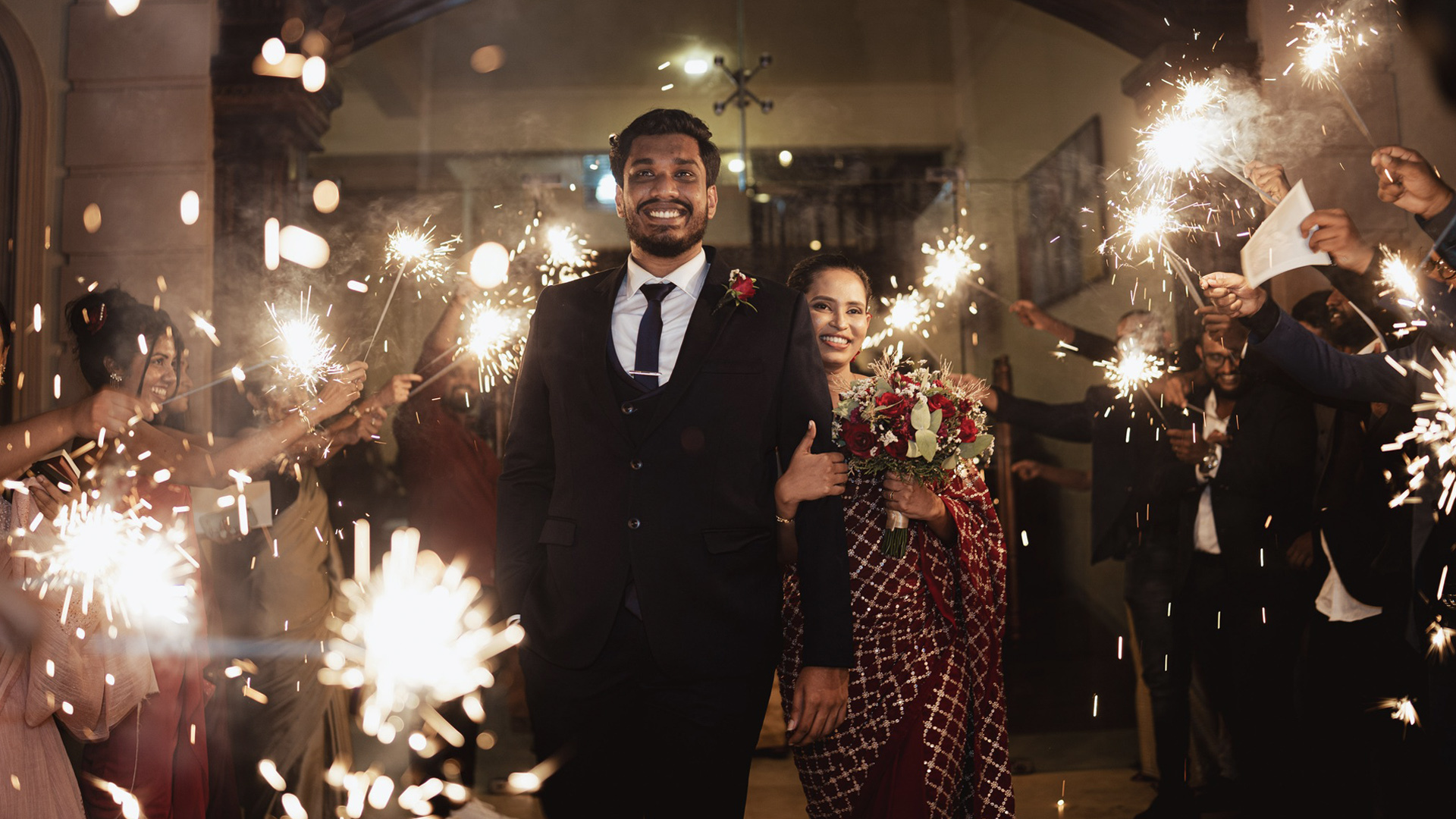 Couple holds hands walking through a sparkler send-off at their wedding, celebrating love and marriage in Sri Lanka, featured on Poruwa.lk | ශ්‍රී ලාංකීය මංගල යෝජනා, Mangala Yojana, Sri Lanka matrimony, and top marriage proposals.