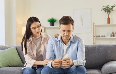  A man and woman sit comfortably on a couch in a living room, engaged in conversation amidst a welcoming atmosphere.