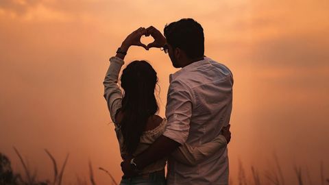 A couple forming a heart shape with their hands against a vibrant sunset backdrop, representing love and togetherness in SriLanka matrimony and matrimony Sri Lanka, celebrating marriage proposals Sri Lanka, and the joy of a traditional Poruwa ceremony.
