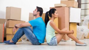 A man and woman sit back-to-back among moving boxes, symbolizing new beginnings while exploring marriage proposals in Sri Lanka through a wedding proposal website, Mangala Yojana, Sri Lankan matrimony, and planning a traditional Poruwa ceremony for Lanka brides and grooms.