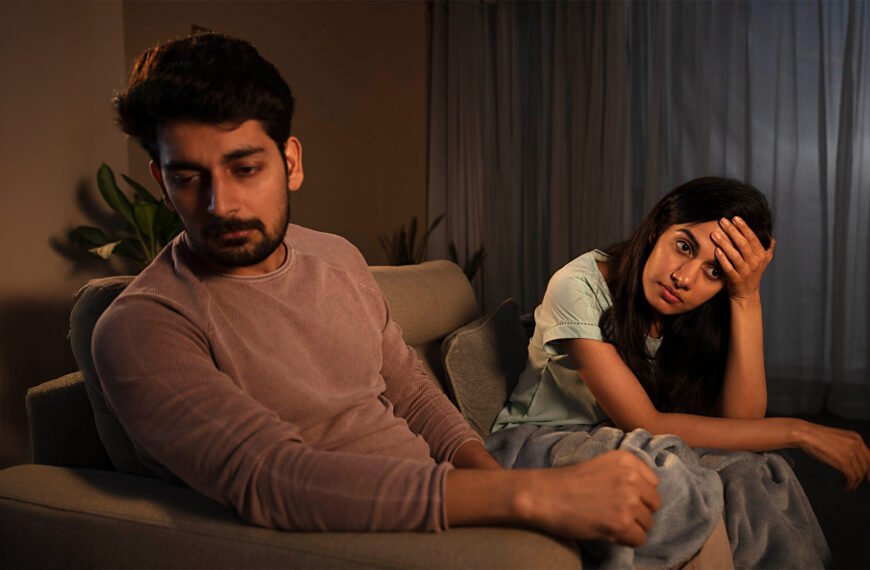 A man and woman sit on a couch looking upset and distant, with the woman holding her head and the man looking away, representing challenges in Sri Lanka matrimony and matrimony Sri Lanka. This reflects issues in marriage proposals Sri Lanka, marriage proposals in Sri Lanka, and the emotional stress couples may face when using a wedding proposal website or mangala yojana services before a Poruwa ceremony.