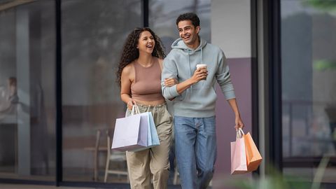 A man and woman stroll down the street, each carrying shopping bags, representing togetherness in SriLanka matrimony, matrimony Sri Lanka, planning marriage proposals Sri Lanka, and preparing for a joyful Poruwa ceremony on Poruwa.lk | ශ්‍රී ලාංකීය මංගල යෝජනා.
