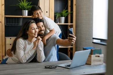  A family smiles together while taking a selfie with their laptop in a cozy living room setting.
