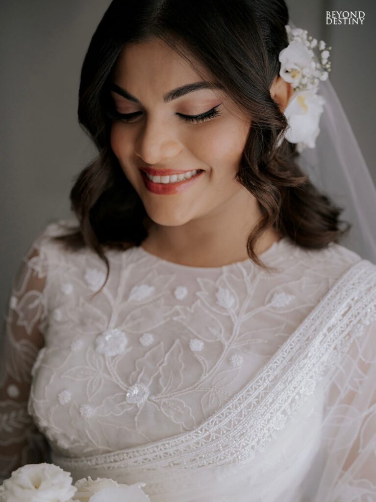 Smiling bride with wavy hair adorned with white flowers, wearing an elegant white dress with floral embroidery in a joyful and serene wedding setting, representing Sri Lankan matrimony, matrimony Sri Lanka, marriage proposal Sri Lanka, marriage proposals in Sri Lanka, marriage proposals Sri Lanka, mangala yojana, wedding proposal website services, and traditional bridal elegance through Poruwa.lk | ශ්රී ලාංකීය මංගල යෝජනා.
