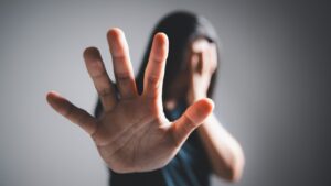 Woman with long hair covering her face and holding a hand in a stop gesture, representing hidden violence against women in Sri Lanka during marriage proposals, mangala yojana, poruwa.lk | ශ්‍රී ලාංකීය මංගල යෝජනා, poruwa ceremony, and matrimony traditions.
