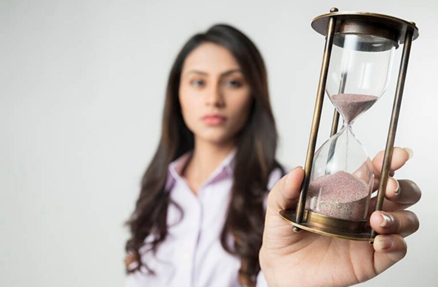 A woman holding an hourglass filled with sand, symbolizing time, patience, and important life decisions such as marriage.