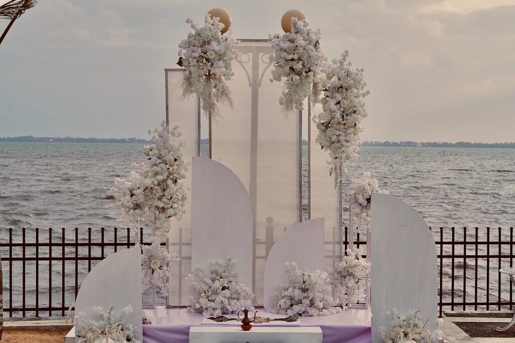Elegant floral wedding arch decorated with white flowers by a lakeside, creating a romantic setting for matrimony Sri Lanka weddings, Poruwa ceremony celebrations, marriage proposals in Sri Lanka, and lanka brides and grooms events.