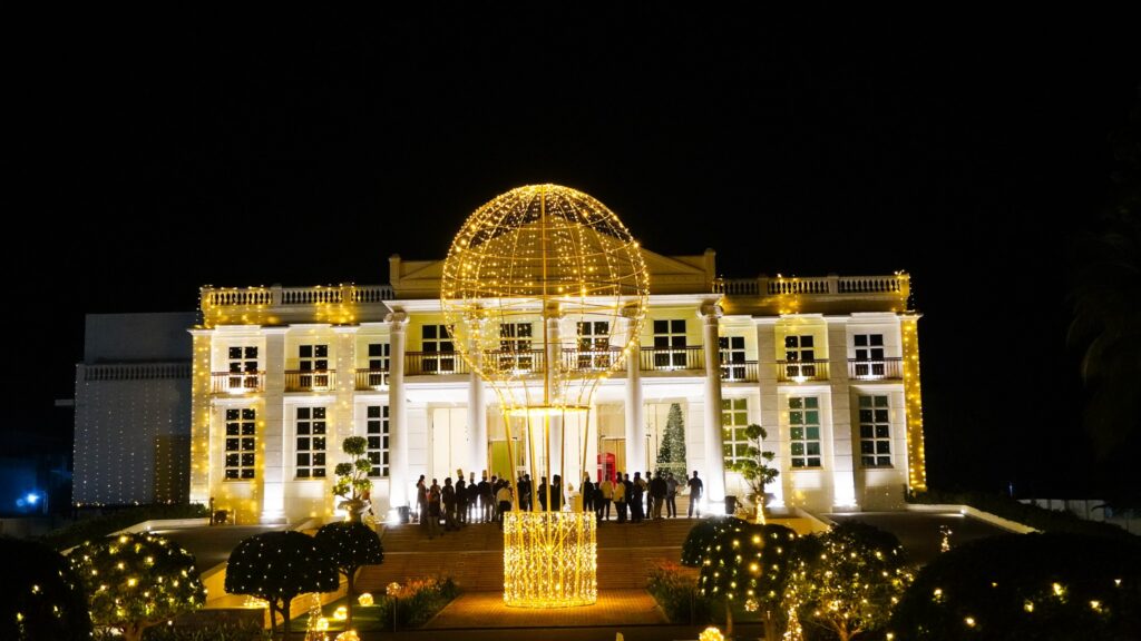 A grand illuminated mansion at night with elegant lighting and guests gathered on the steps, showcasing a luxury venue ideal for matrimony Sri Lanka weddings, Poruwa ceremony celebrations, marriage proposals in Sri Lanka, and lanka brides and grooms events.