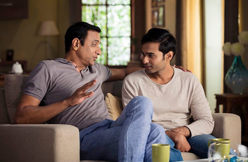 Two Sri Lankan men engaged in a thoughtful conversation while sitting on a couch in a cozy living room, discussing marriage proposals and family matters.