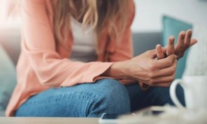 A thoughtful woman sitting on a couch indoors, hands on her knees, looking ahead reflectively, symbolizing contemplation, focus, and personal reflection.