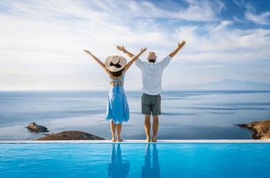Couple in a pool joyfully raising their arms, enjoying a sunny day together.
