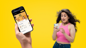 A woman holding a smartphone against a bright yellow background, smiling and looking at the device.