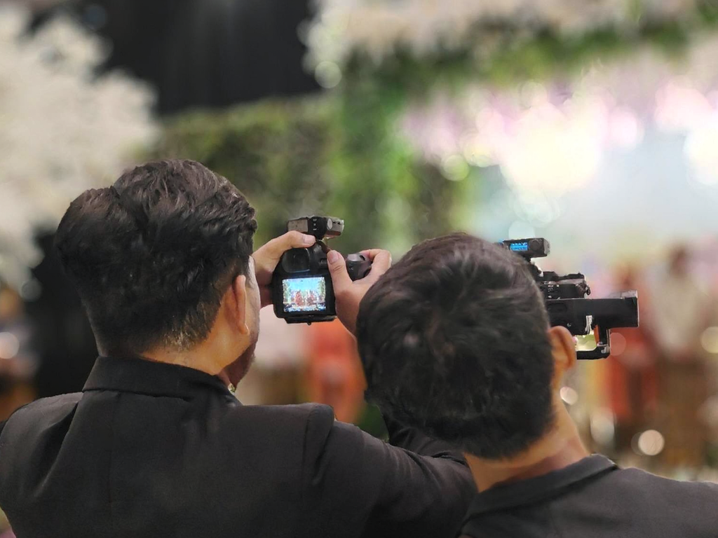Two men photographing a couple exchanging vows during a traditional poruwa ceremony, capturing a memorable moment of Sri Lankan wedding traditions and mangala yojana.
