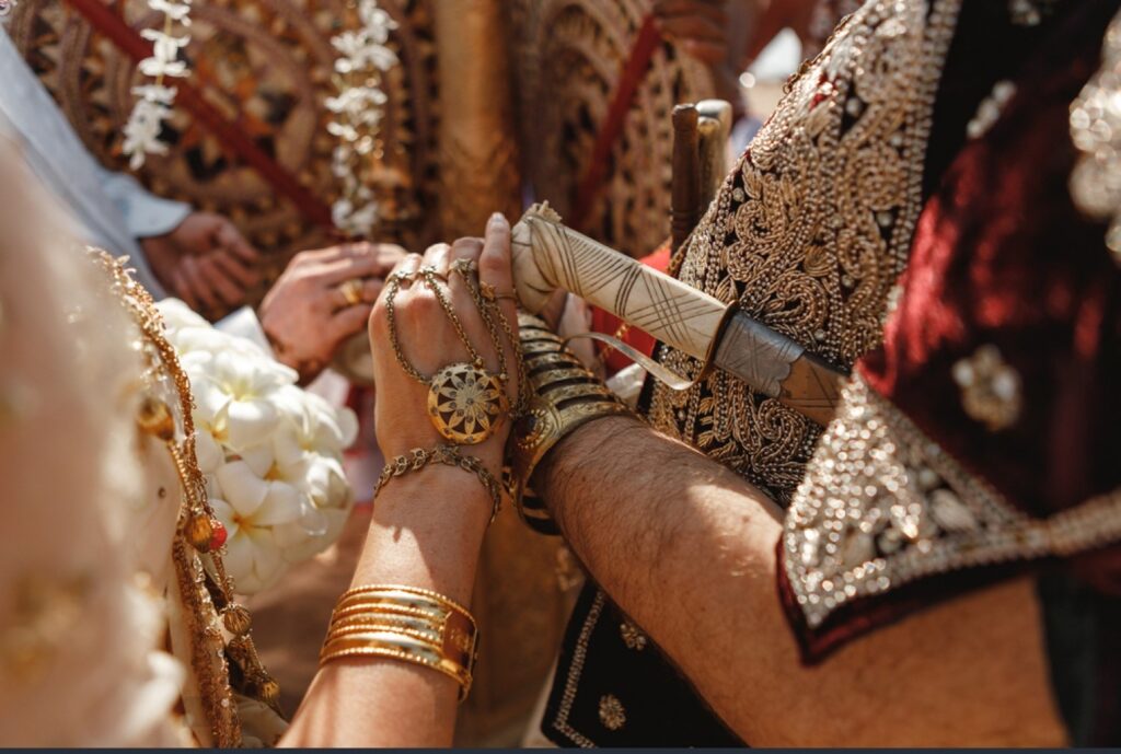 Close-up of hands in ornate traditional Sri Lankan wedding attire holding a decorated ceremonial sword during a poruwa ceremony, featuring gold jewelry and detailed embroidery that reflect mangala yojana customs and Sri Lankan wedding traditions showcased on Poruwa.lk | ශ්‍රී ලාංකීය මංගල යෝජනා, a trusted wedding proposal website for marriage proposal Sri Lanka, marriage proposals in Sri Lanka, matrimony Sri Lanka, Sri Lanka matrimony, Buddhist matrimony, Catholic marriage proposals, Lanka brides and grooms, LankaMatrimony, Purahanda LK, Hitad marriage proposals, and Liyathabara marriage proposals in Sri Lanka.