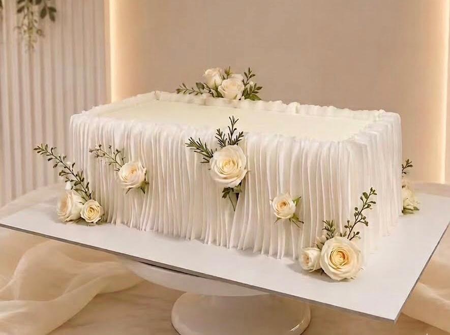 Elegant white wedding cake decorated with pink roses on a white tablecloth, representing Sri Lankan wedding traditions, mangala yojana, marriage proposals in Sri Lanka, matrimony Sri Lanka, srilanka matrimony, and wedding celebrations for Sri Lankan brides and grooms.